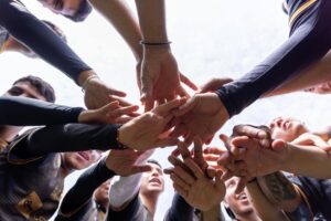 Servicios A diverse group of athletes join hands in a team huddle, symbolizing unity and motivation.