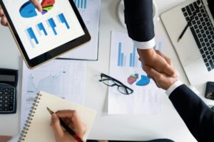 Servicios Business professionals handshake over graphs and charts in a corporate setting, symbolizing successful negotiation and agreement.