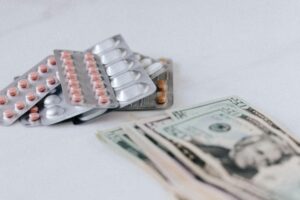 Servicios Multicolored pills in silver blisters on white surface near heap of paper money representing expensive pharmacy
